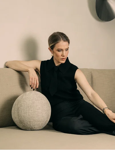 doctor Emily Deane in black sleeveless dress sitting on beige sofa with round decorative pillow in minimalist interior - in Montreal, QC
