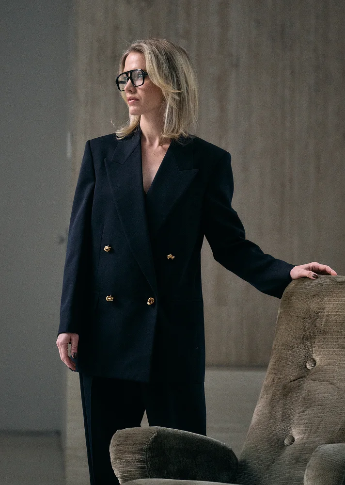 Doctor Emily Deane in black double-breasted blazer dress standing beside modern concrete furniture in minimalist interior - Doctor in Montreal, QC