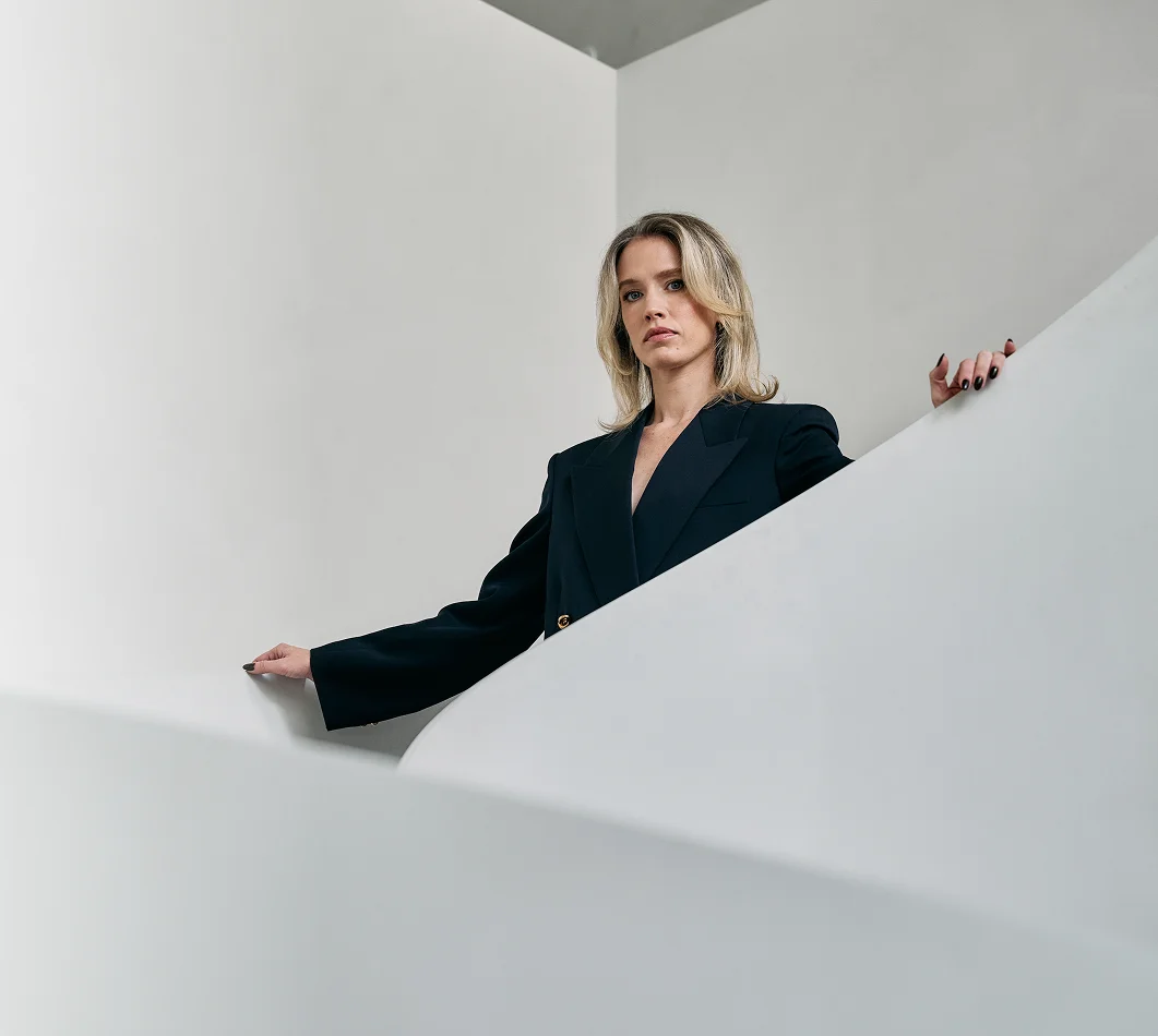 Doctor Emily Deane in black blazer standing on modern white staircase with minimalist architectural design - in Montreal, QC