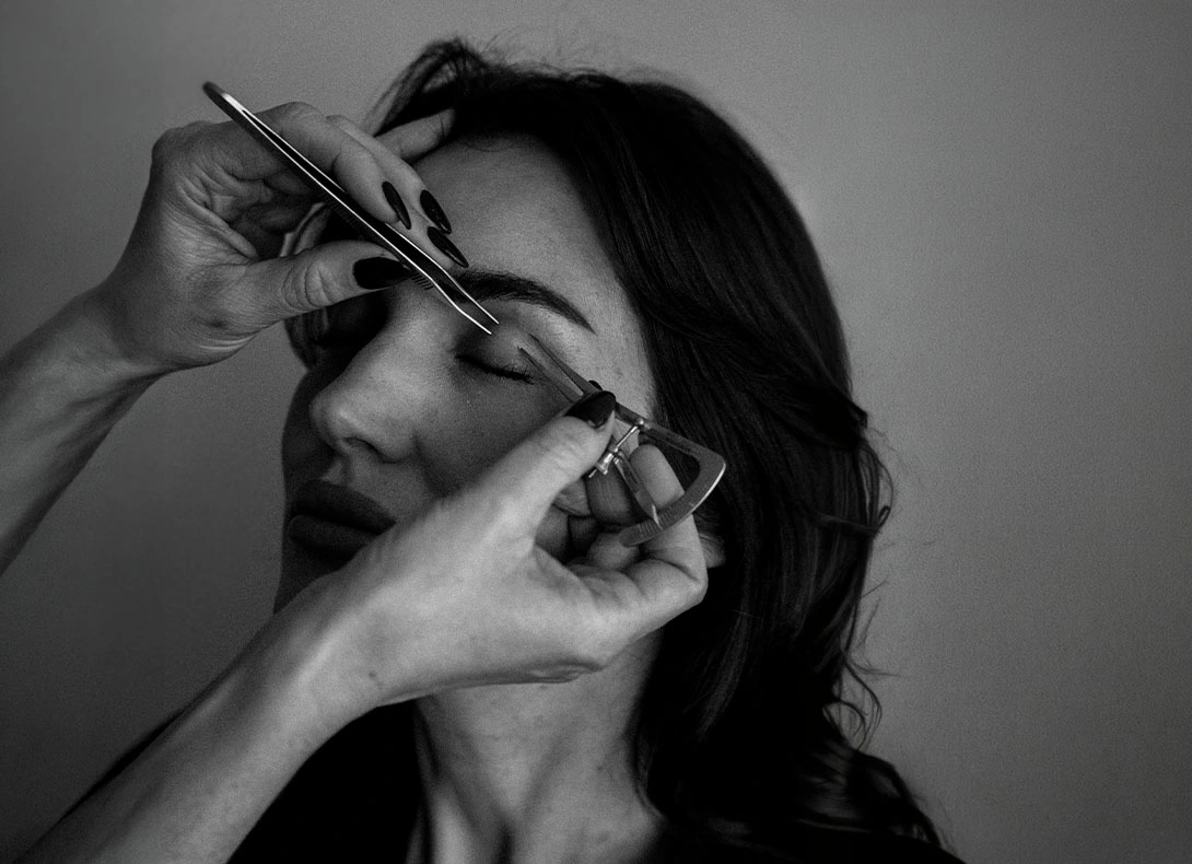 Woman examining her upper eyelids with fingers while looking at camera in black and white photograph. - Upper eyelid surgery in Montreal, QC