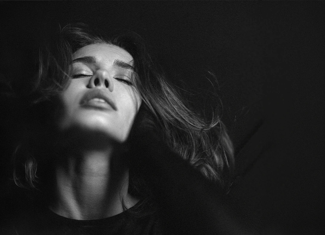 Black and white portrait of woman with flowing hair in dramatic side lighting and shadow. - Chin implant surgery in Montreal, QC