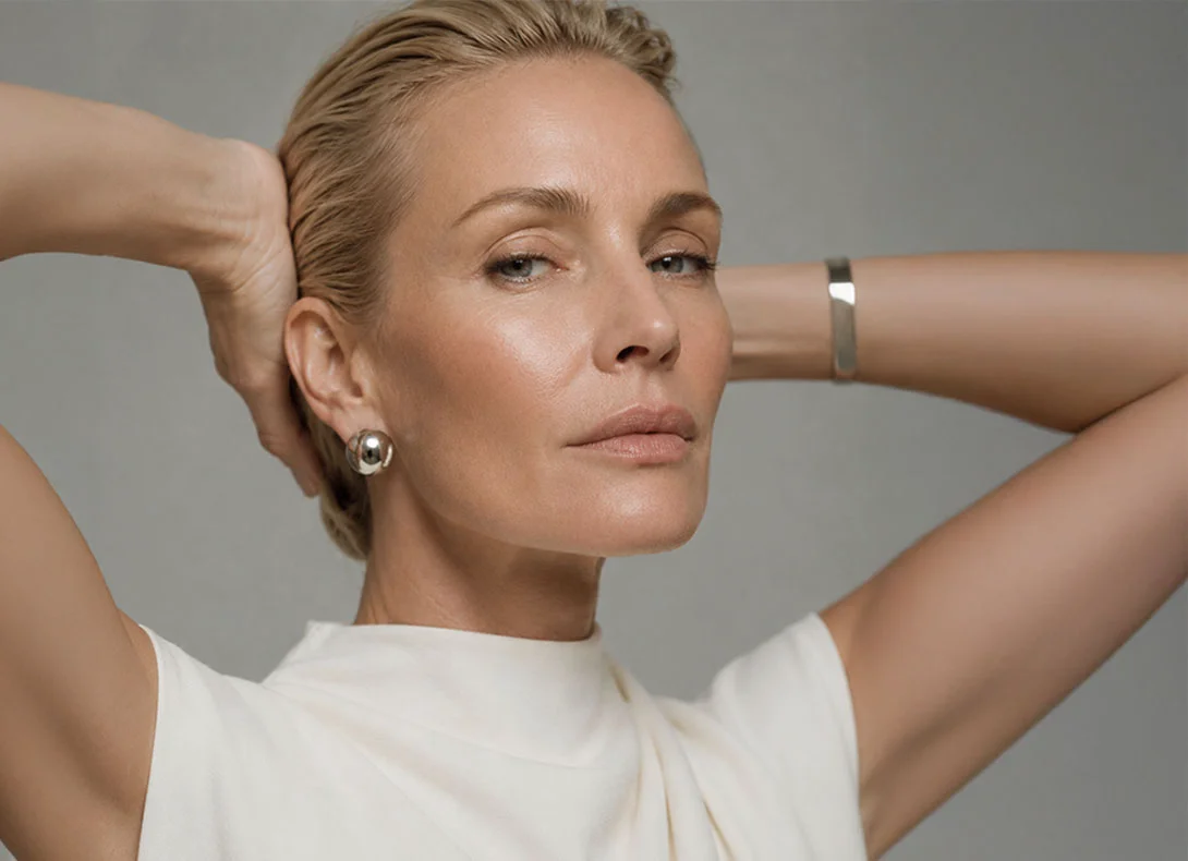 Elegant blonde woman in white sleeveless top with hands behind head against neutral background - Facelift in Montreal, QC