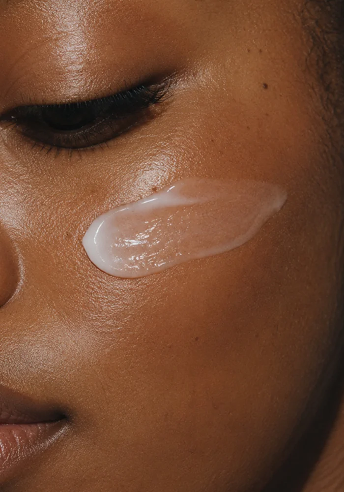 Woman applying white facial cream or moisturizer to glowing brown skin on cheek - skin in Montreal, QC