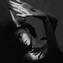 Black and white portrait of woman with graceful pose stretching arms above head against dark background - Brow lift in Montreal, QC