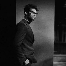 Professional man in business attire with glasses standing in contemplative pose against textured wall - Hair transplant in Montreal, QC