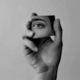 Hand holding mirror reflecting eye, symbolizing self-examination and eyelid surgery consideration in black and white - lower eyelid surgery in Montreal, QC
