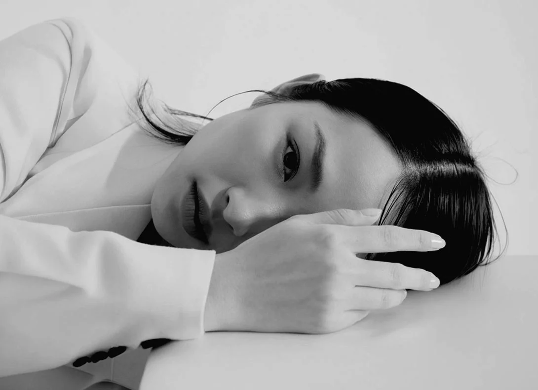 Woman lying down showcasing natural Asian eyelid features in black and white portrait - Asian eyelid surgery in Montreal, QC