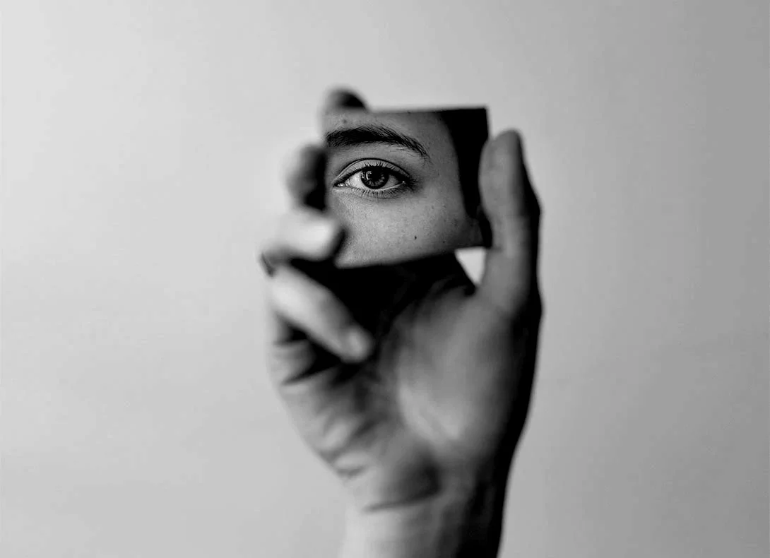 Hand holding mirror fragment reflecting person's eye in black and white composition - Lower eyelid surgery in Montreal, QC